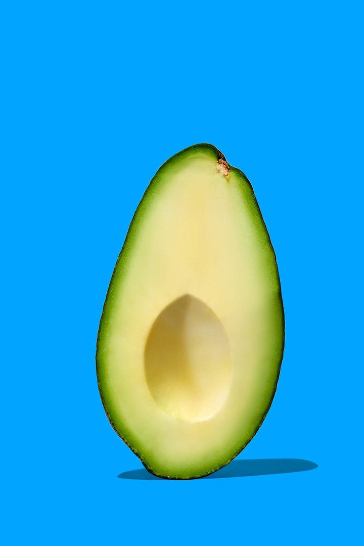 Halved avocado with stone removed, standing upright against a bright blue background