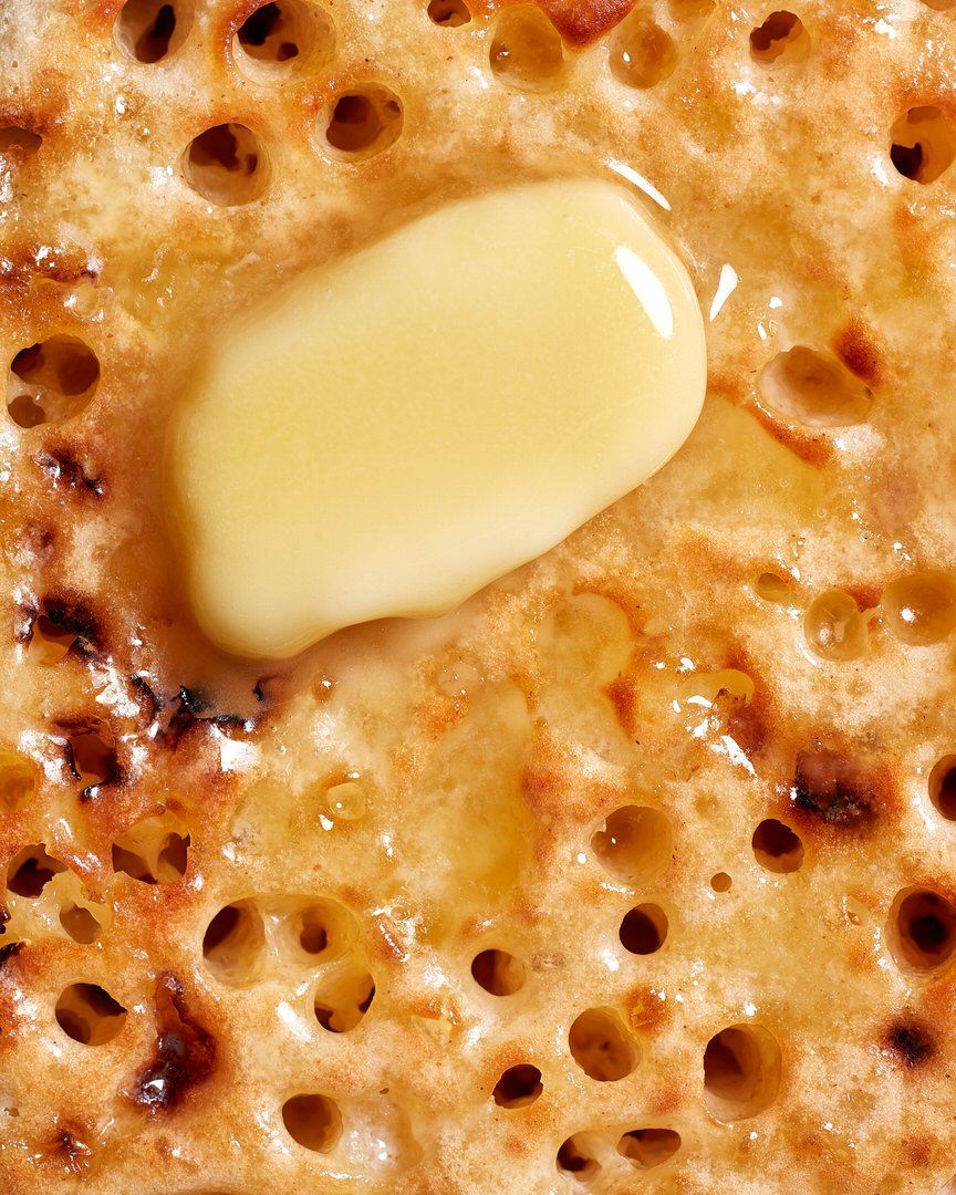 Close-up of a melting knob of butter on toasted crumpet, showing its characteristic holes