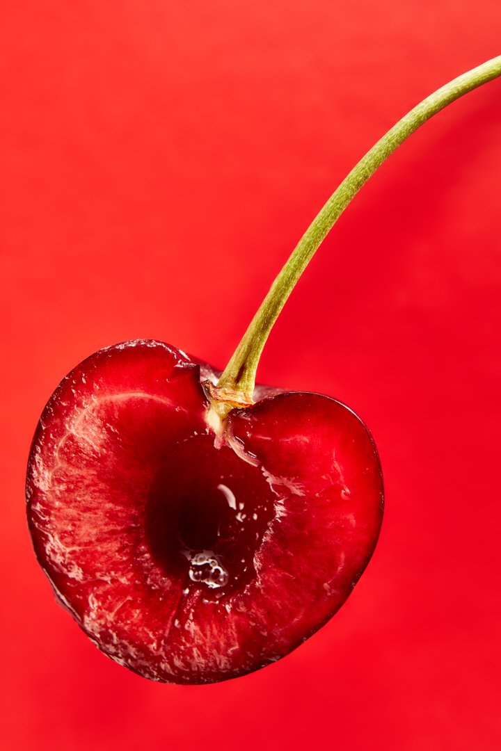 Close-up of a halved cherry with its stem, pit removed, against a red background