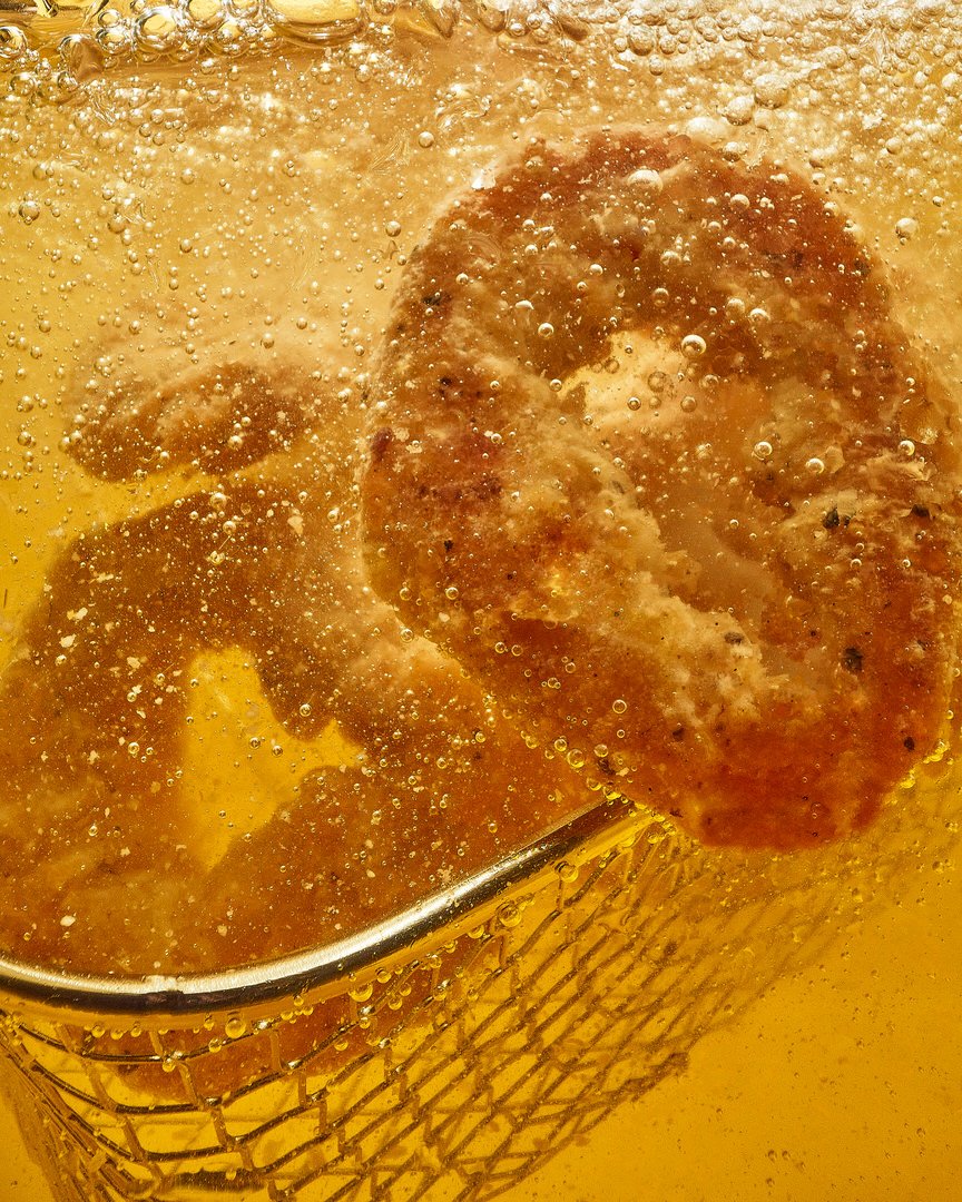 Breaded meat cutlets deep-frying in bubbling oil in a wire fryer basket