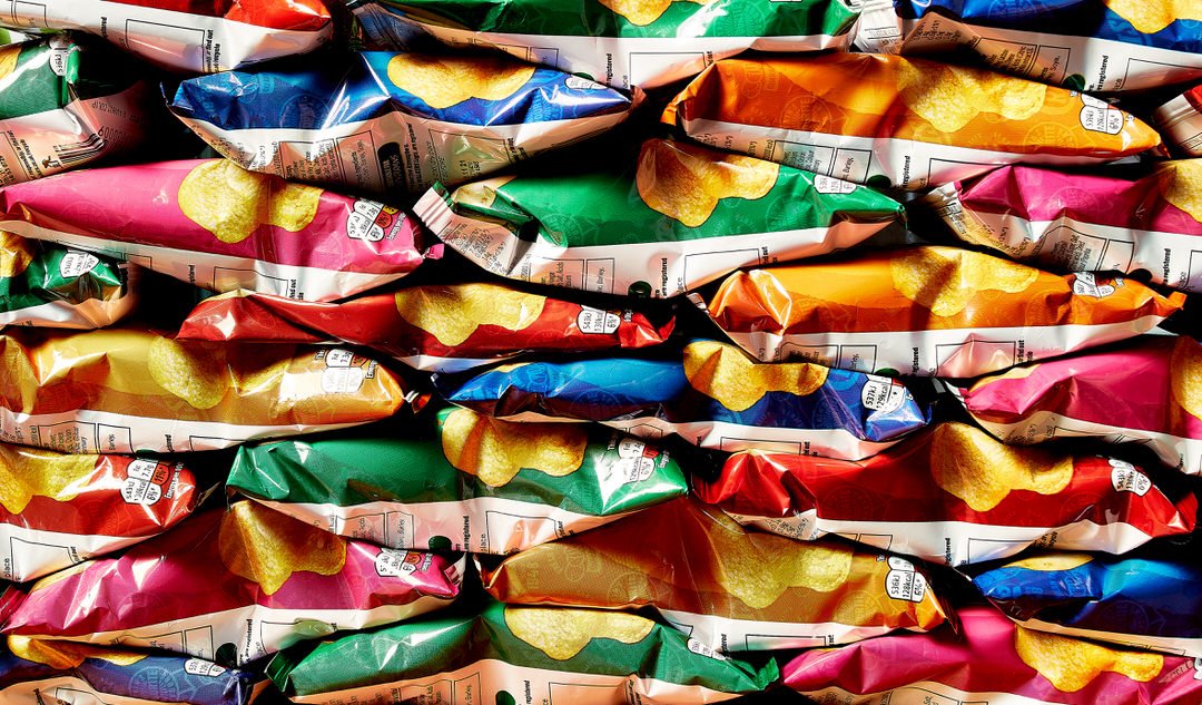 Rows of colourful crisp packets stacked closely together, each showing a crisp graphic and price label
