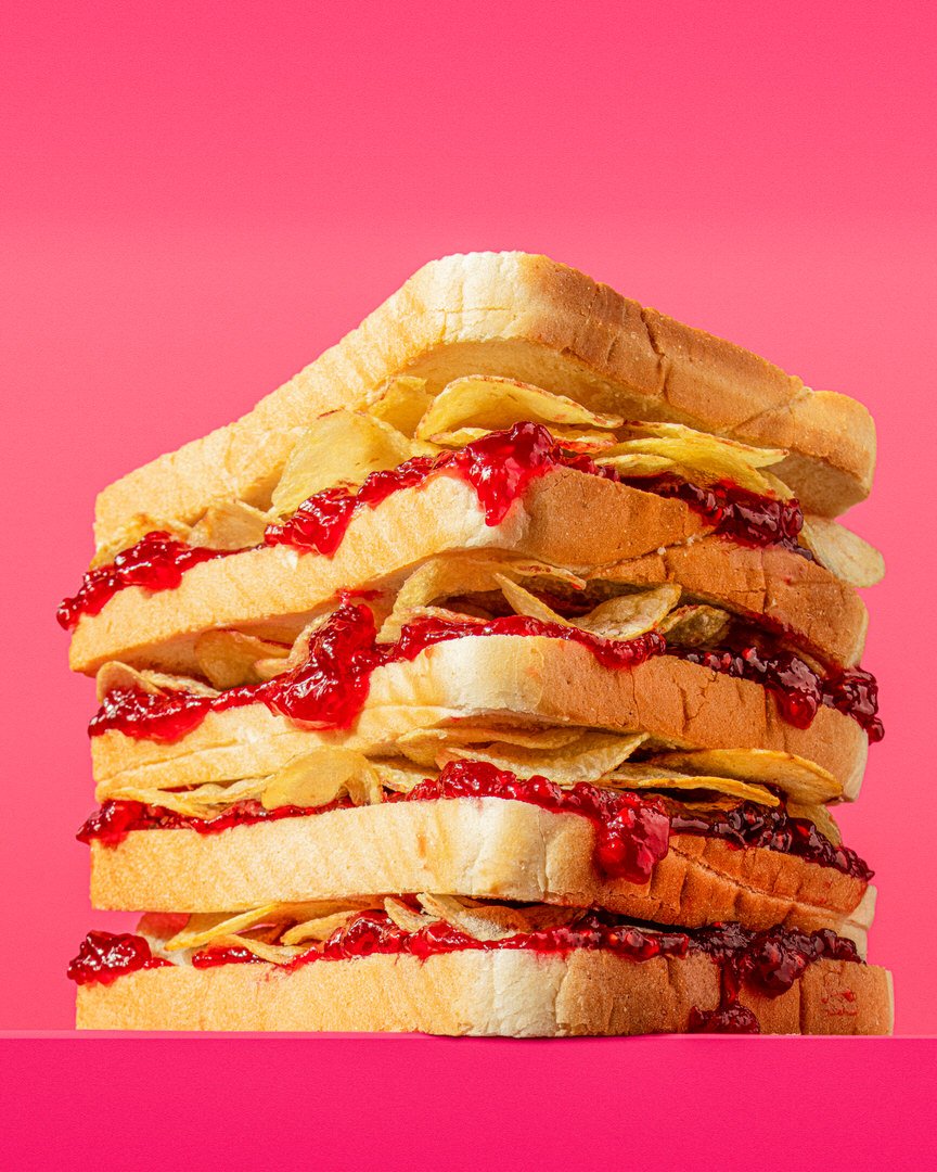 Stack of white bread sandwiches layered with jam and crisps, against a bright pink background