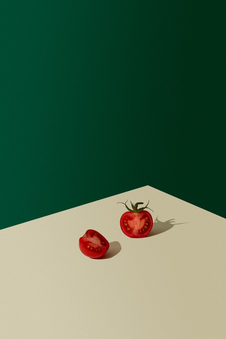 Two halved tomatoes on a cream surface against a dark green background