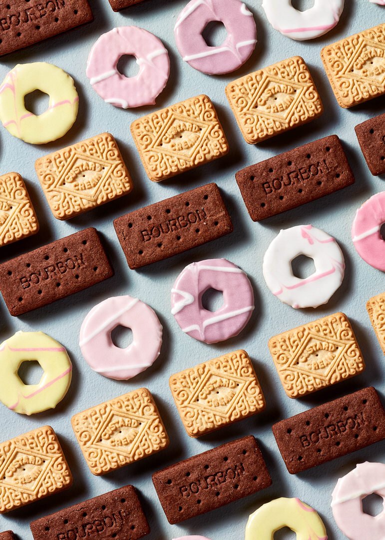 Rows of Bourbon and custard cream biscuits arranged with pink, white and yellow iced ring biscuits