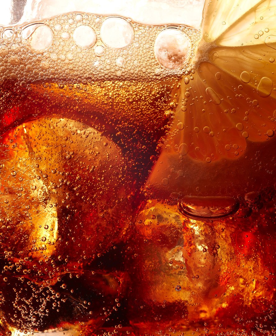 Close-up of fizzy cola with ice cubes and a lime slice, bubbles rising to the surface