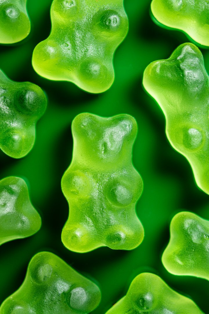 Close-up of green gummy bear sweets arranged closely together on a green background