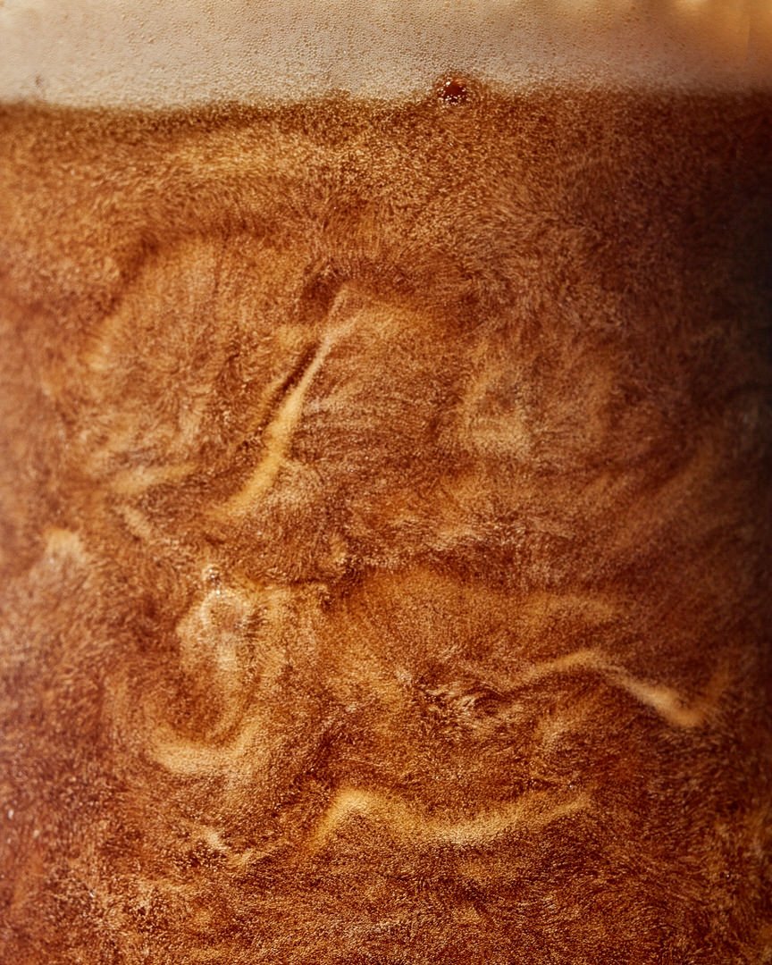 Close-up of a dark beer with swirling foam patterns rising through the amber-brown liquid