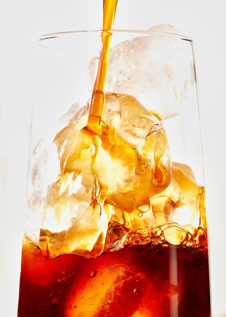 Close-up of dark cola being poured over ice cubes in a tall glass