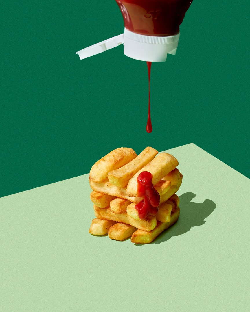 Ketchup bottle dripping sauce onto a stacked pile of chips against a green background