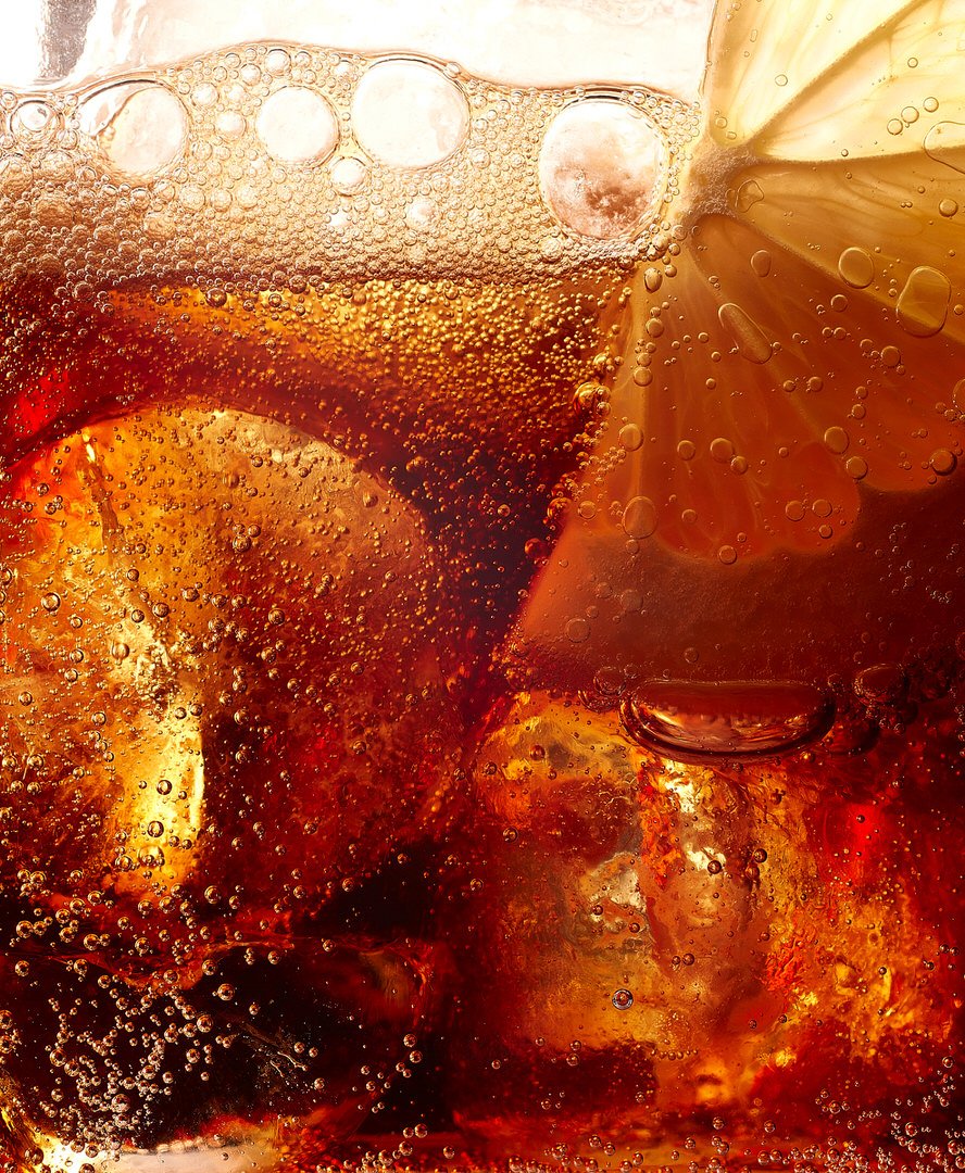 Close-up of fizzy cola with ice cubes and a lemon slice, bubbles rising through the dark amber liquid