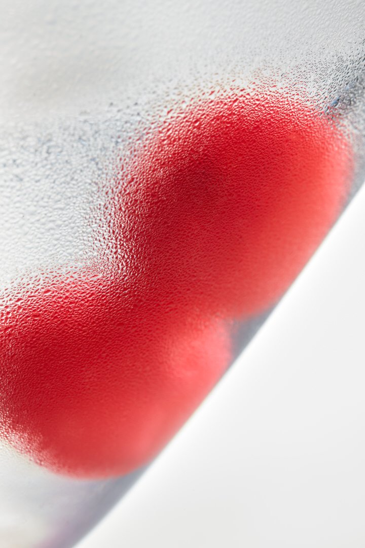 Close-up of red fruit shapes seen through a condensation-covered glass surface