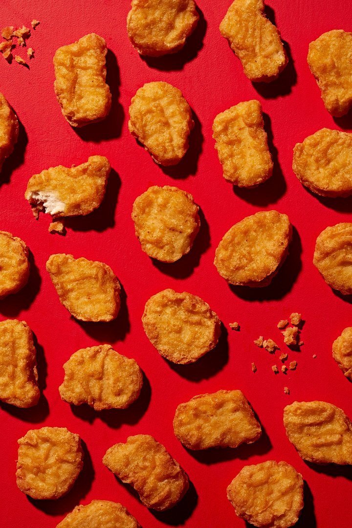 Rows of golden breaded chicken nuggets arranged on a red background, one bitten to show the inside