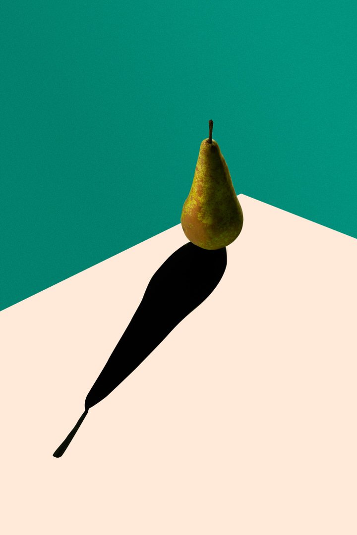 A single pear casting a long dramatic shadow against a teal and cream background