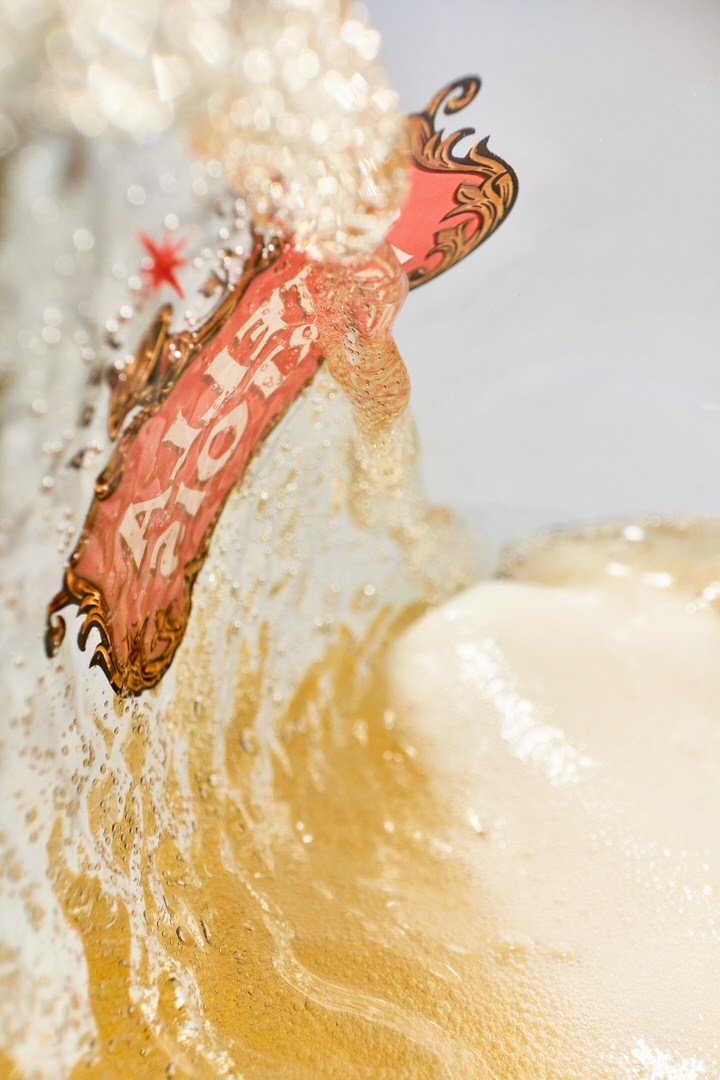 Close-up of golden beer overflowing with foam, label pressed against the glass, bubbles rising through the liquid