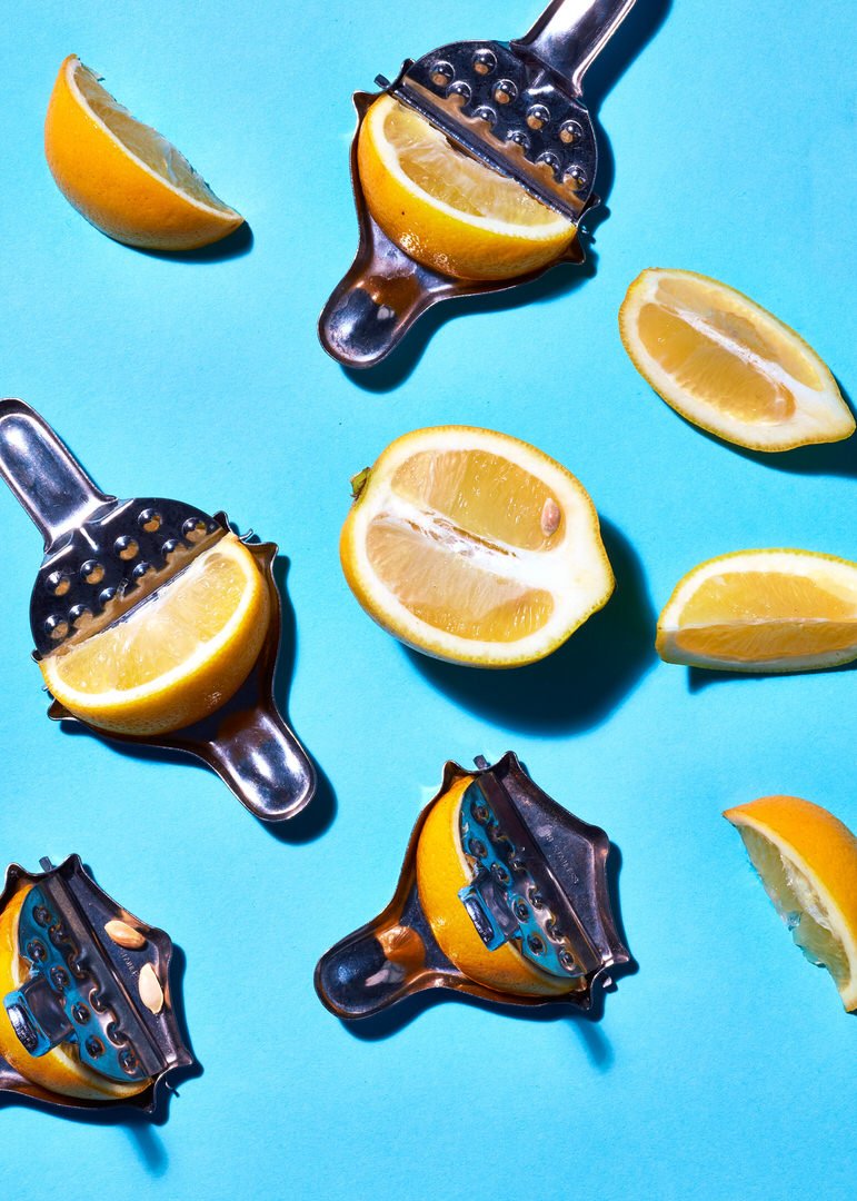 Citrus juicers gripping halved oranges and lemons, arranged with loose wedges on a bright blue background