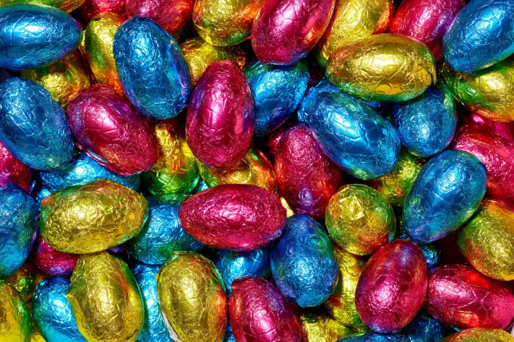 Small chocolate eggs wrapped in blue, pink, gold and green foil, piled together