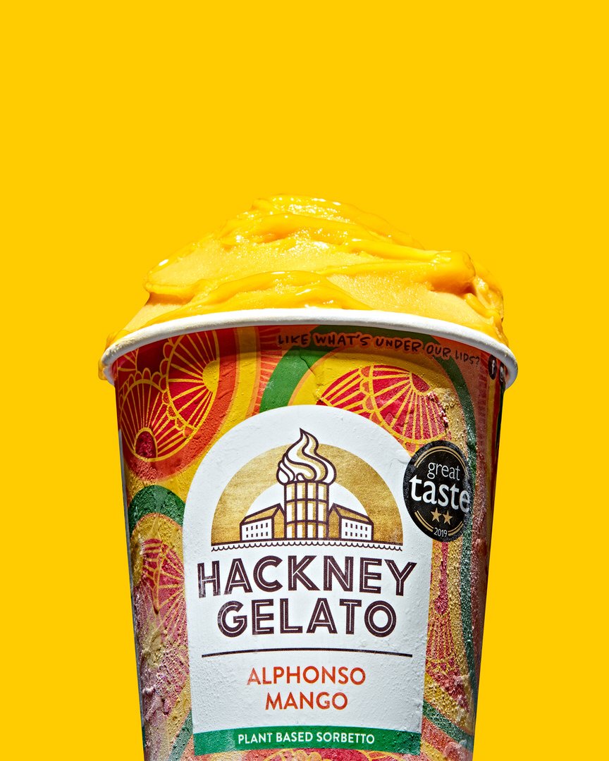 Tub of Hackney Gelato Alphonso Mango plant-based sorbetto, topped with a swirl of mango sorbet, on a yellow background