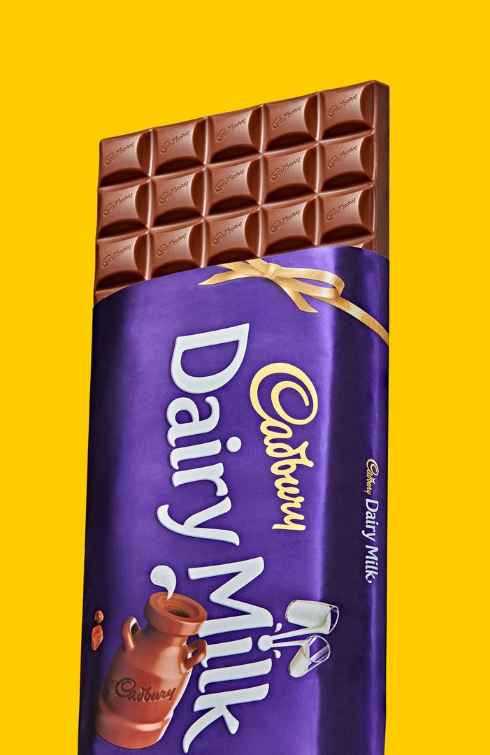 Cadbury Dairy Milk chocolate bar, unwrapped at the top, on a yellow background