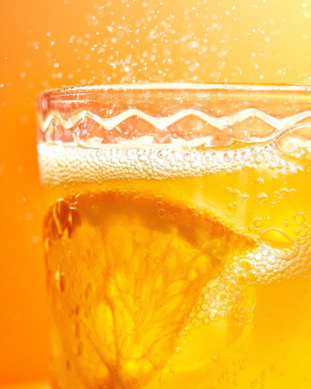 Close-up of a fizzy orange drink in a glass, with a citrus slice and rising bubbles