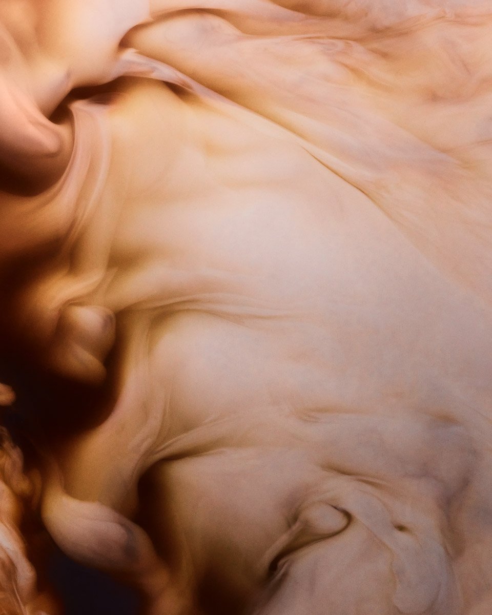 Abstract close-up of swirling amber and cream-coloured smoke or liquid forming soft, flowing shapes
