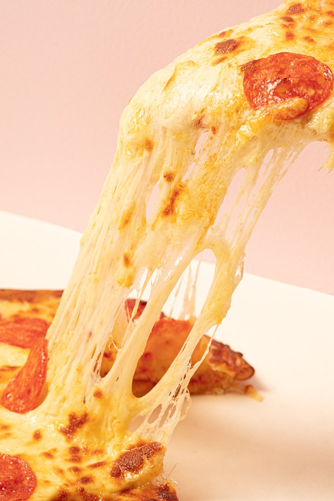 Slice of pepperoni pizza lifted from the pie, with melted cheese stretching in long strings