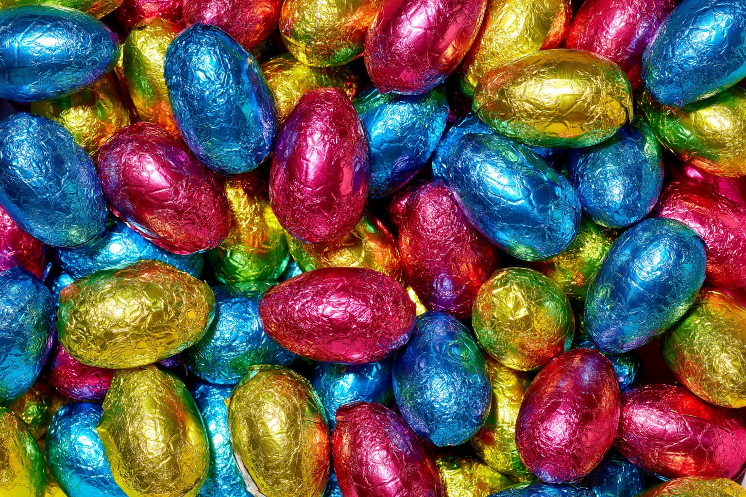 Mini chocolate eggs wrapped in shiny blue, pink, yellow and green foil, piled together