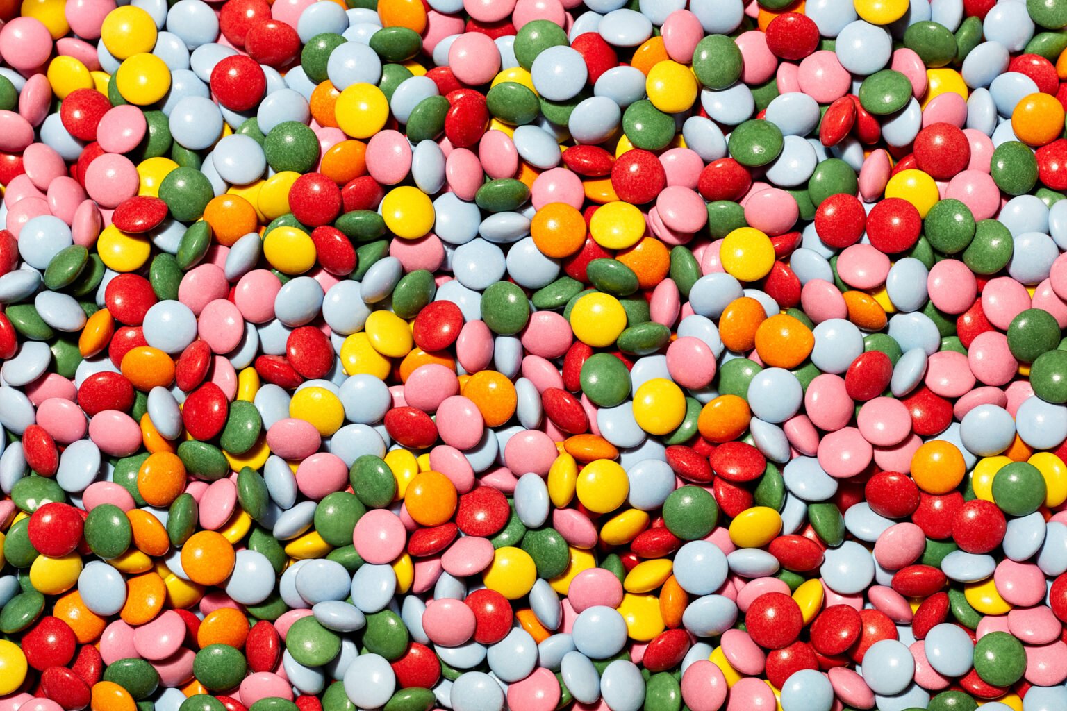 Close-up of a large pile of colourful, chocolate button-style sweets in red, yellow, green, pink, orange and pale blue