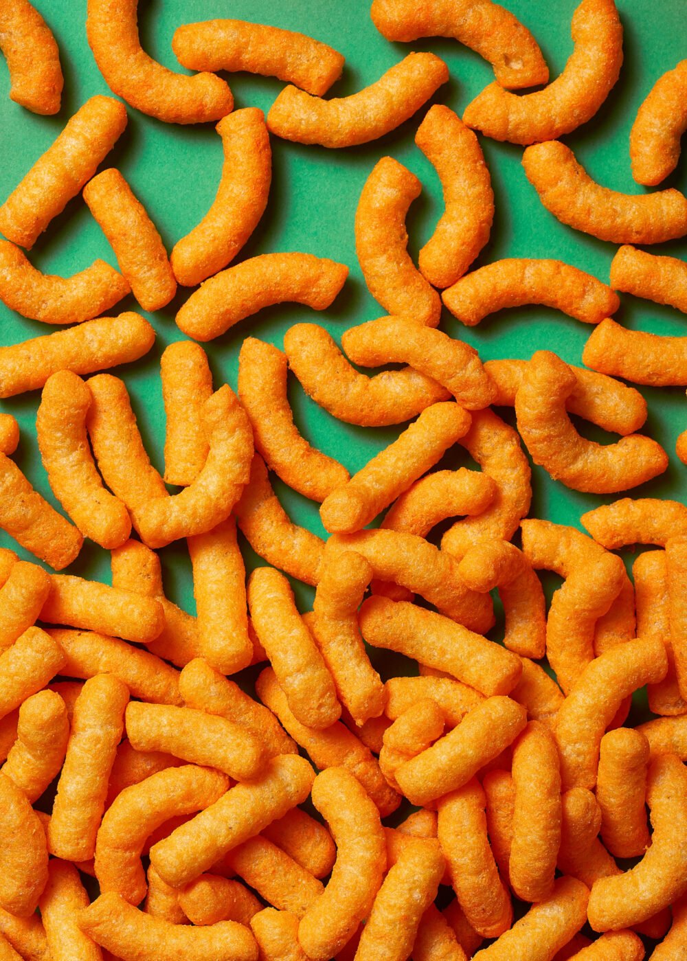 Curly orange cheese puff snacks scattered across a green surface