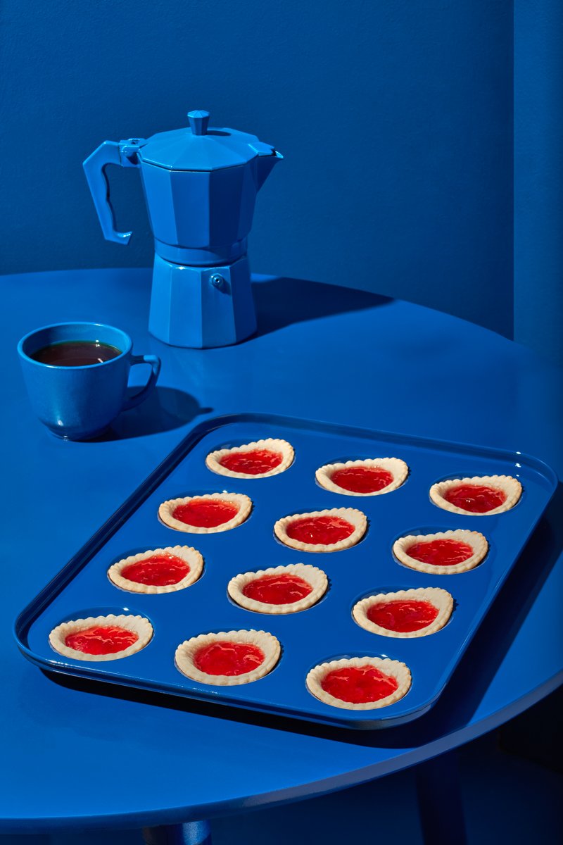 A tray of jam tarts beside a coffee cup and stovetop moka pot, all bathed in blue light