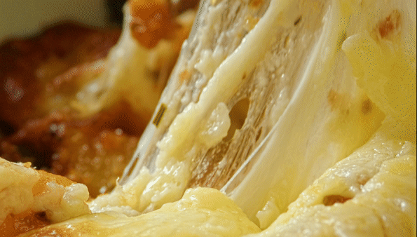 Close-up of melted cheese being pulled into long, stretchy strings over a baked dish