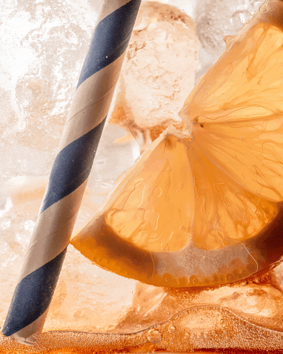 Close-up of an orange slice and striped straw in an iced drink
