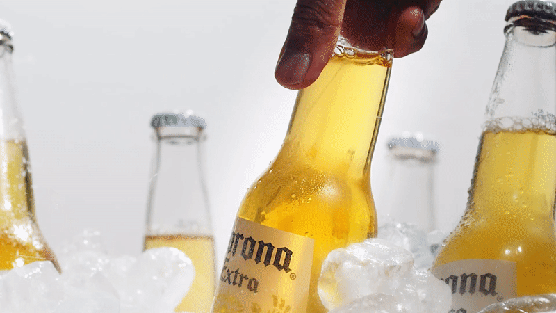 A hand pulls a chilled Corona Extra bottle from a bed of ice among other beer bottles