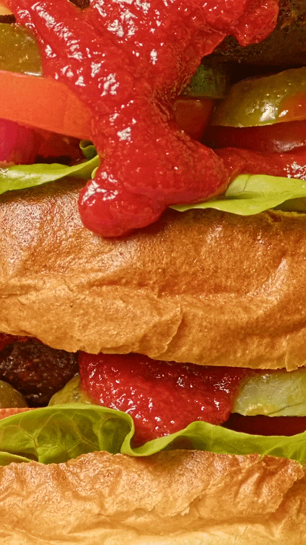 Close-up of a stacked burger with layers of ketchup, lettuce, tomato and bun visible