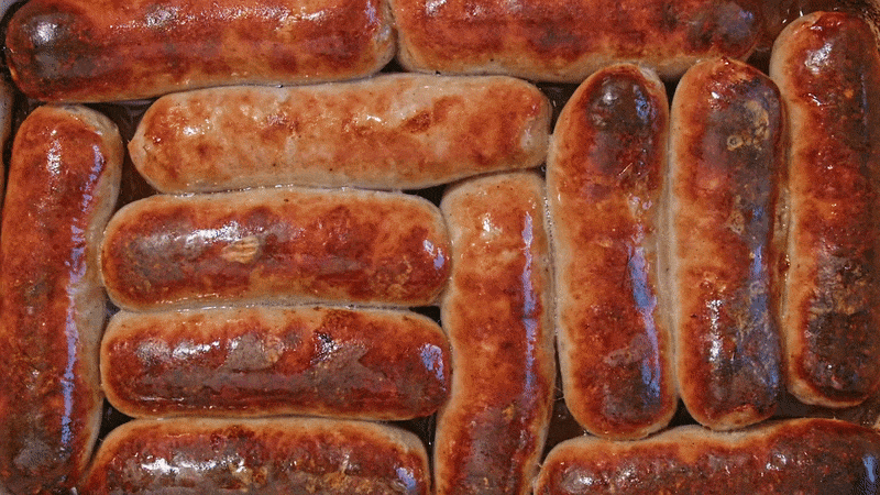 Close-up of golden-brown sausages roasted in a tray, packed tightly together