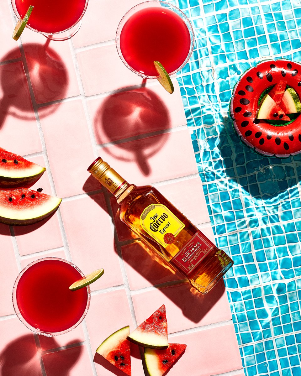 Bottle of Jose Cuervo Especial tequila beside watermelon margaritas, watermelon slices and a pool