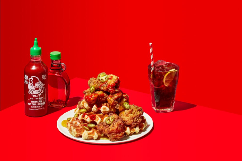 Fried chicken and waffles topped with sriracha and sliced chillies, served with a bottle of Thai Dragon sriracha, maple syrup and an iced cold drink