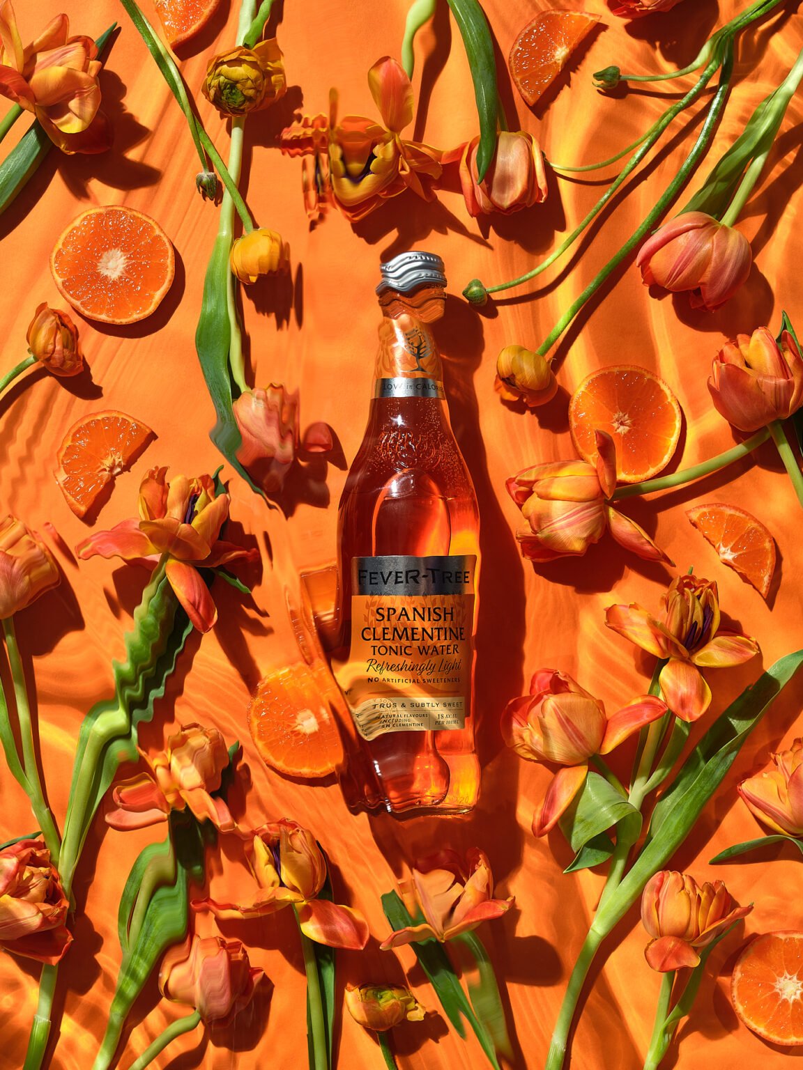 Bottle of Fever-Tree Spanish Clementine Tonic Water surrounded by orange tulips and clementine slices