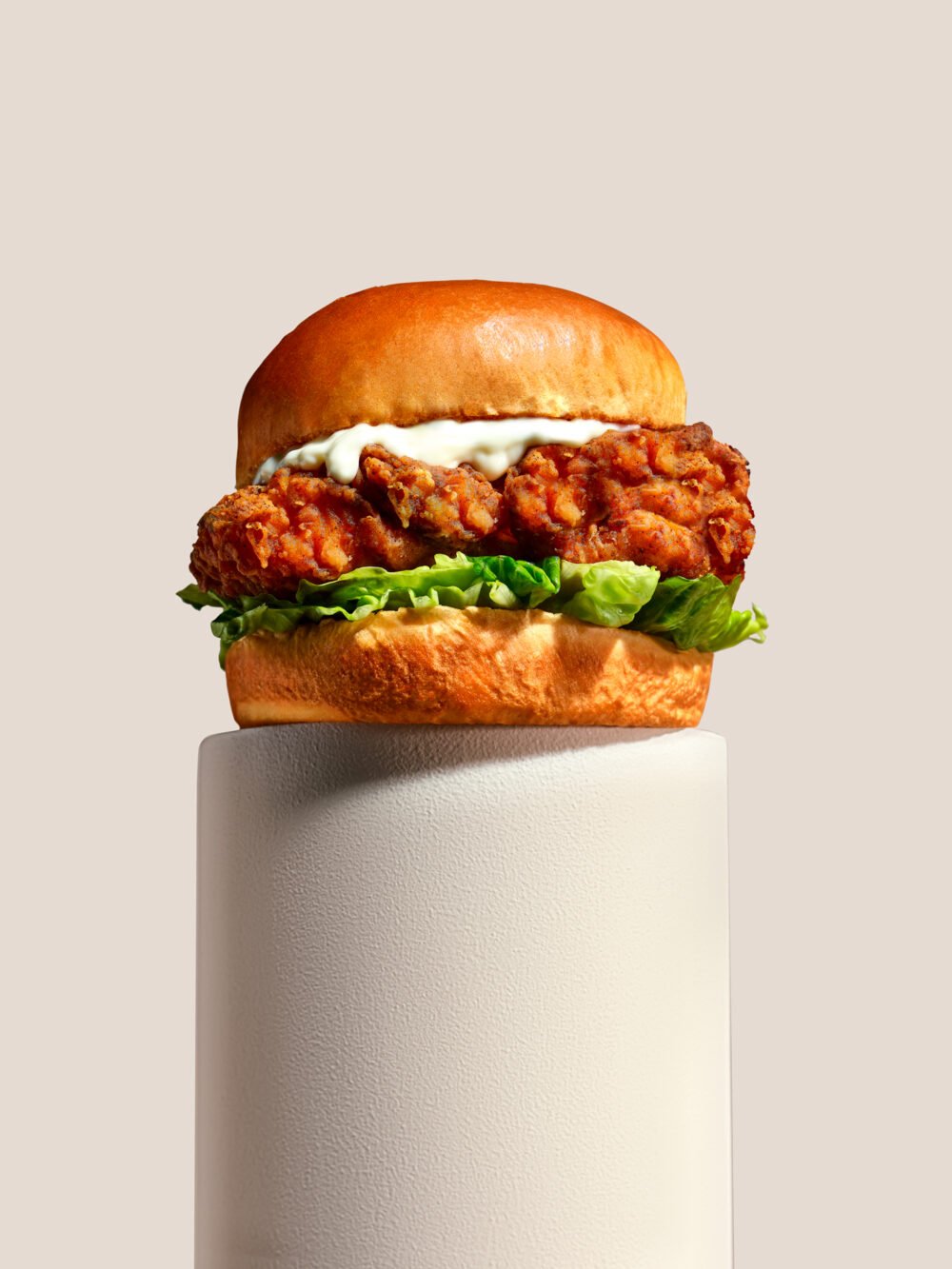 Crispy fried chicken burger with lettuce and creamy sauce in a brioche bun, displayed on a pedestal