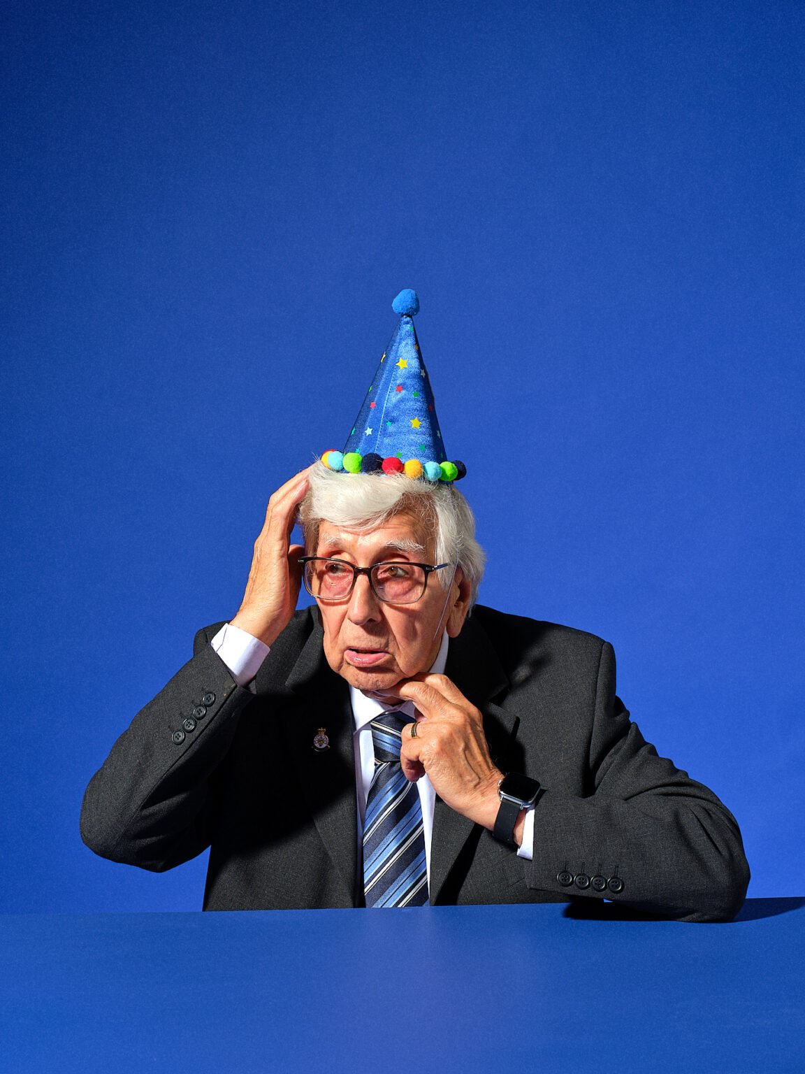 commercial advertising portrait of an old man wearing a party hat photographed on a mid blue set.