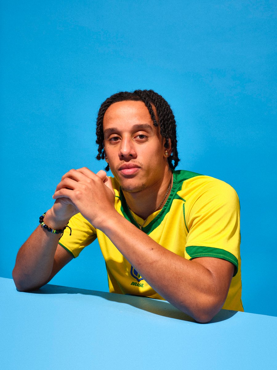 Man wearing a yellow and green Brazil football shirt, leaning on a table against a blue background