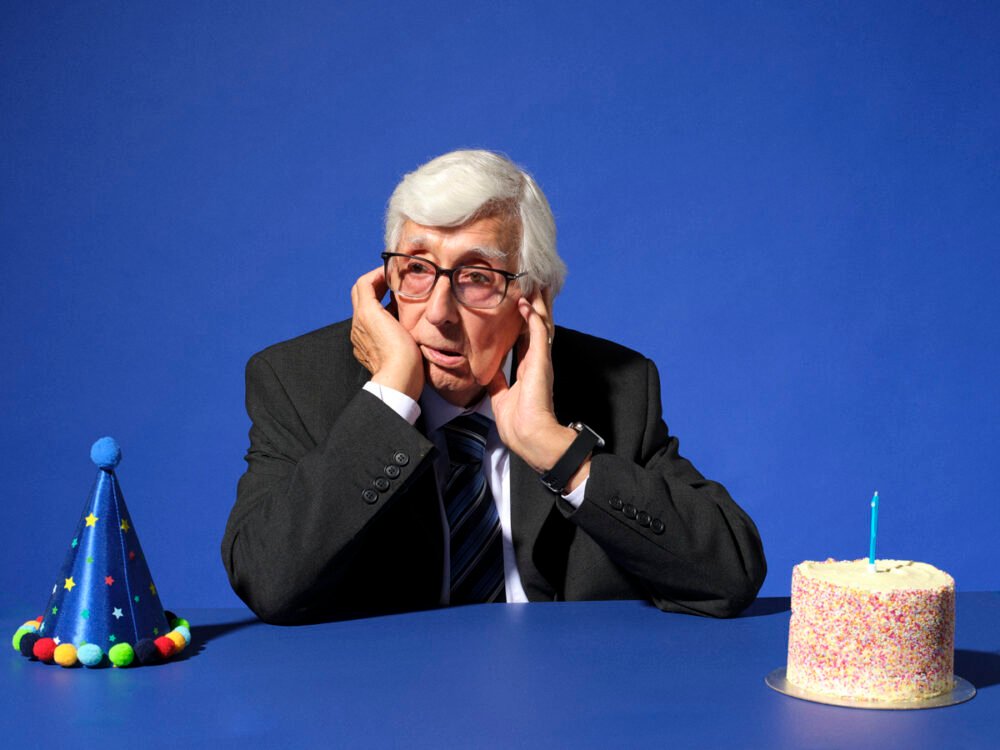 Portrait in a studio by Scott Choucino of an old man in a suit with a birthday cake looking sad