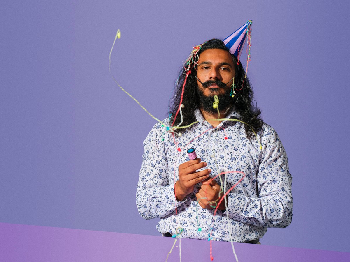 a sad looking man setting of party poppers in a birthday outfit for comedic looking commercial portrait