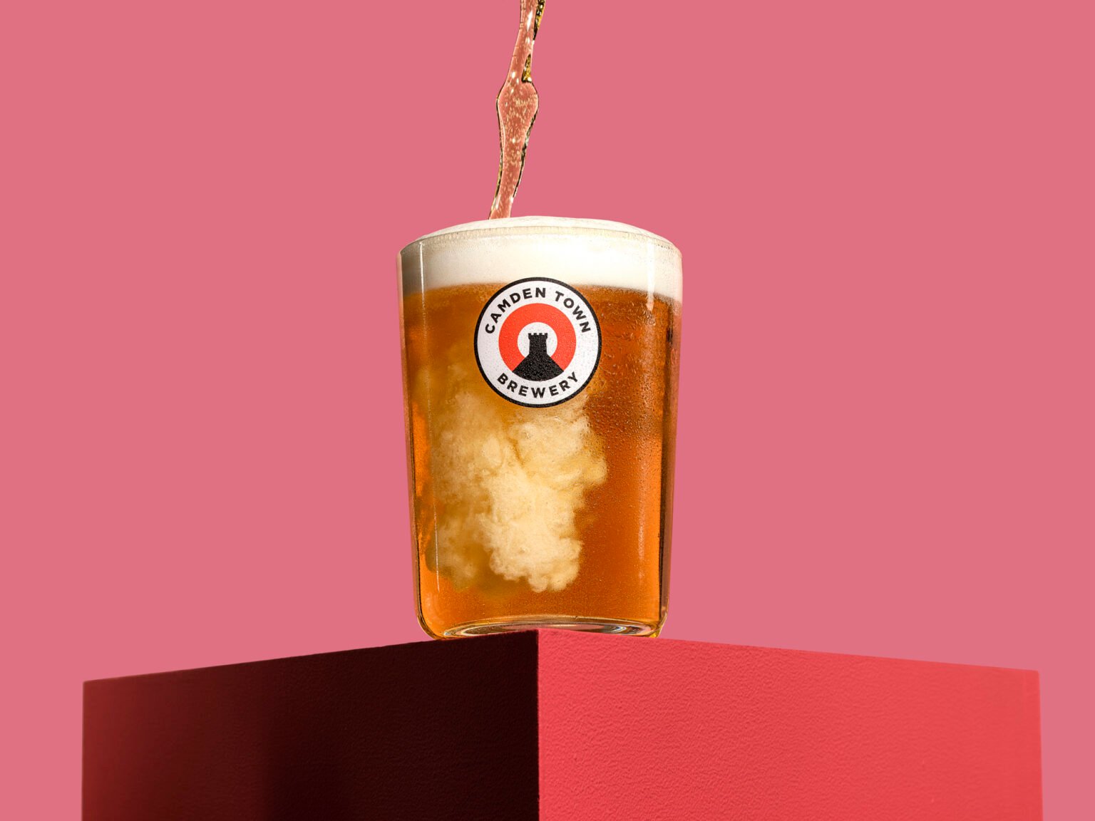 a stylised graphic and bold photograph of beer being poured on a pink set taken by commercial photographer scott choucino