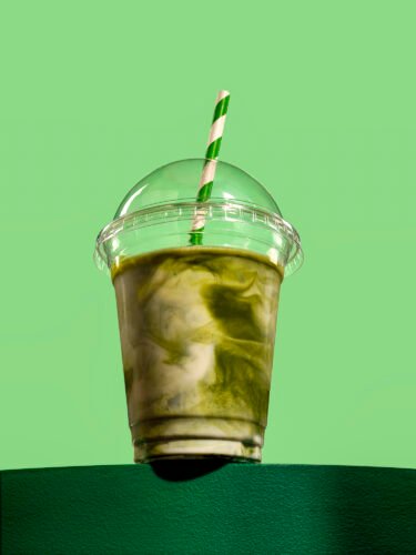 heroic commercial photograph of a matcha coffee drink in takeaway cup on a green background