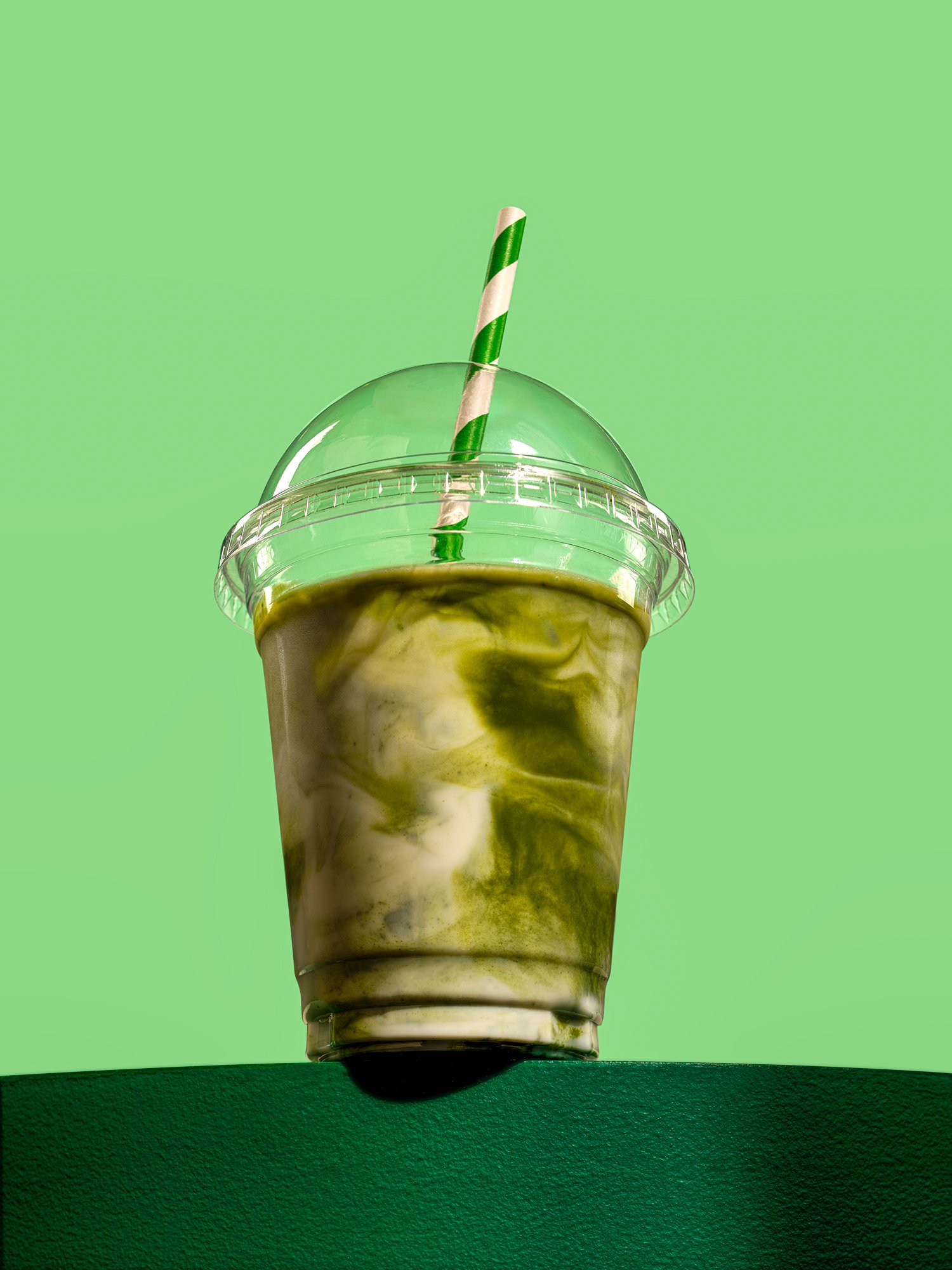 heroic commercial photograph of a matcha coffee drink in takeaway cup on a green background