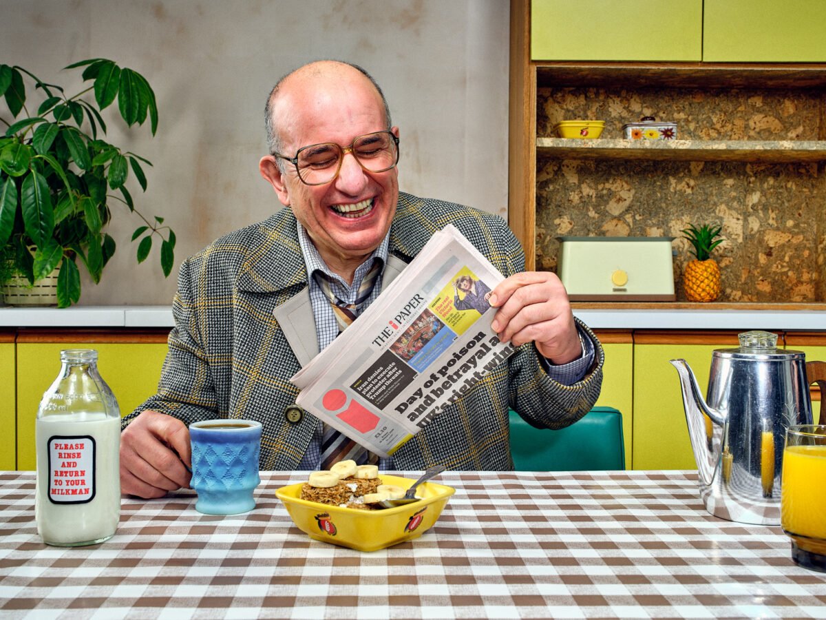 an office worker laughing whilst reading the paper in a photograph taken by commercial photographer scott choucino in a kitchen set built by HK curates