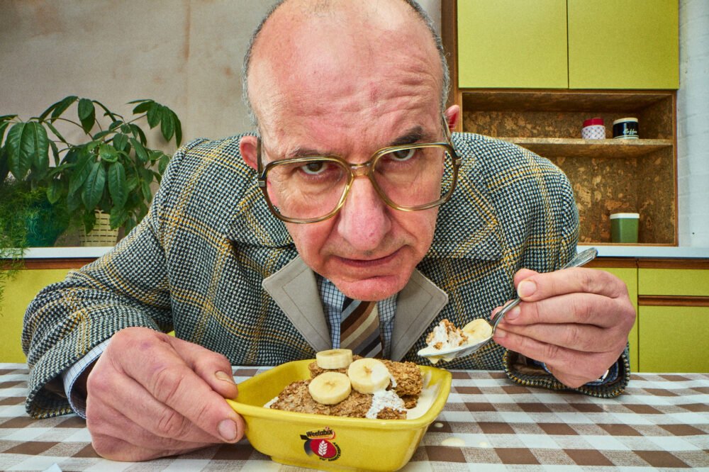 probe lens portrait of man looking straight into camera whilst eating breakfast in a high end vintage kitchen set