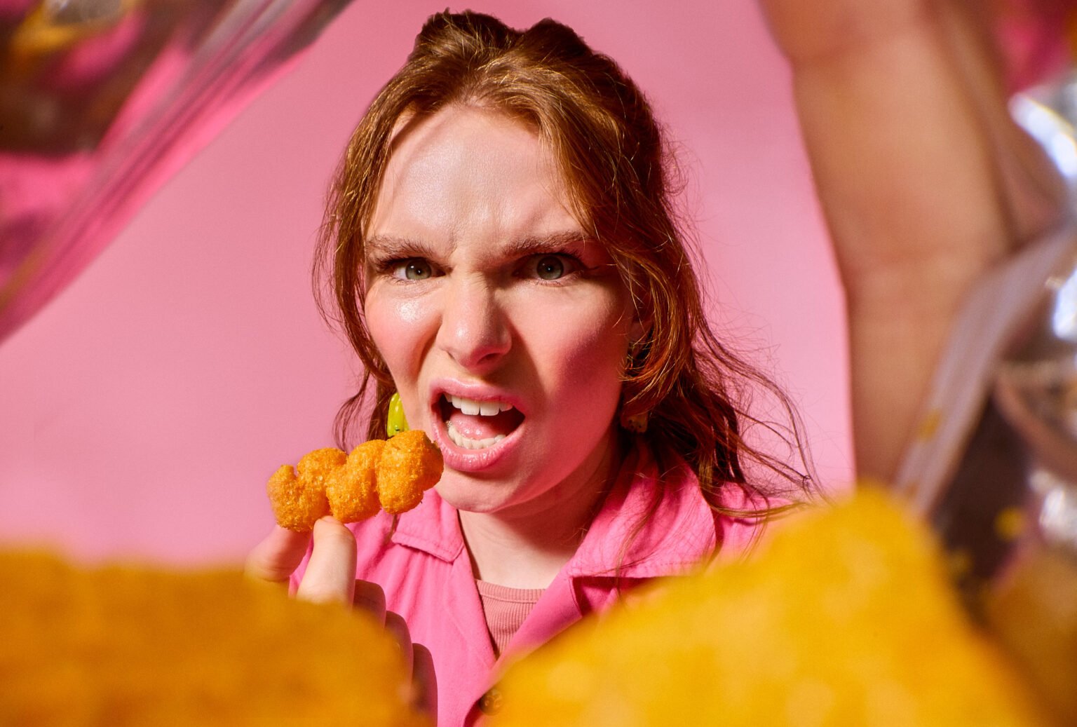 a portrait taken with a laowa probe lens from inside a crisp packet as a lady wearing pink on a pink background eats a crisp