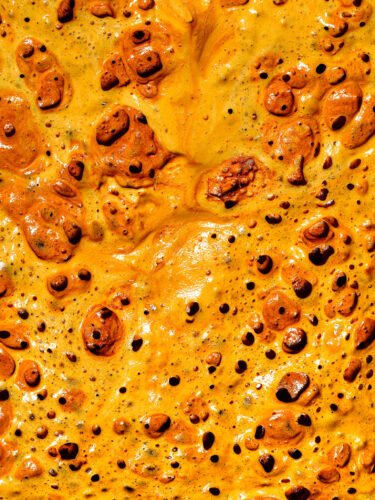 Close-up of a bubbling, caramelised orange-yellow surface with dark blistered pockets, resembling melted cheese or toffee