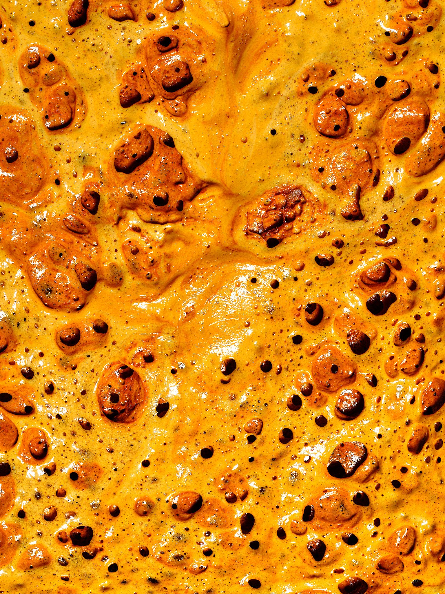 Close-up of a bubbling, caramelised orange-yellow surface with dark blistered pockets, resembling melted cheese or toffee